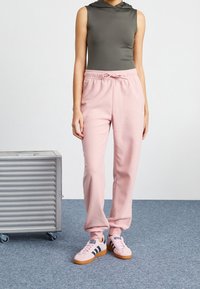 Hooded gray sleeveless top paired with soft pink sweatpants featuring an elastic waistband. Pink sneakers with navy stripes complete the look.