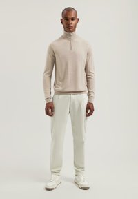 Beige svetr na zip, světlé kalhoty a bílé tenisky. Hladká textura, přiléhavý střih a minimalistická estetika.
