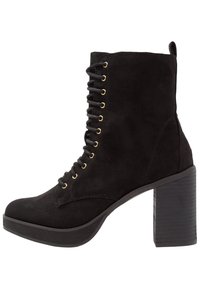 Bottine en daim noir avec œillets dorés, design à lacets, et talon épais en bois. Bout rond et surface texturée.