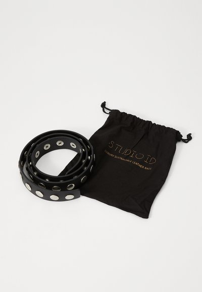 Sort læderbælte med cirkulært sølvhardware, snoet ved siden af en sort trækpose med guldtekst "STUDIOID" og "LUXURY SUSTAINABLE LEATHER BAGS."