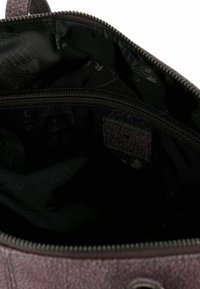 Interior texturizado de color púrpura oscuro de una bolsa con cierre de cremallera. Presenta un forro negro en contraste y pequeños detalles de marca.