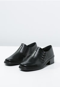 Black leather slip-on shoes with a rounded toe, a low block heel, and decorative metal accents on the sides. Smooth texture.