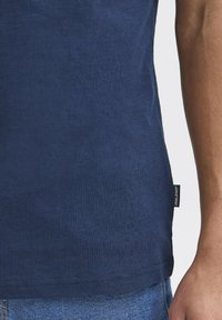 Tums zila īsām piedurknēm t-kreklam, izgatavots no gludas kokvilnas ar nedaudz fakturētu virsmu, ar šūtu etiķeti apakšējā pusē.