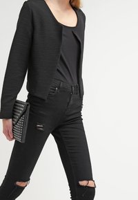 Svart ribbad croppad jacka över en svart topp, tillsammans med slitna svarta skinny jeans. Håller en nitar prydnad svart clutch.