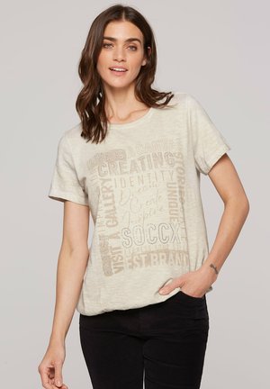 Hellbeige T-Shirt mit kurzen Ärmeln und strukturiertem Druck mit verschiedenen Wörtern und Phrasen in dunkleren Farbtönen. Rundhalsausschnitt und lockere Passform.