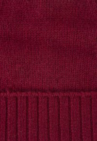 Burgundy knitted beanie with a textured, ribbed design and a soft, warm appearance. Material appears thick and elastic.