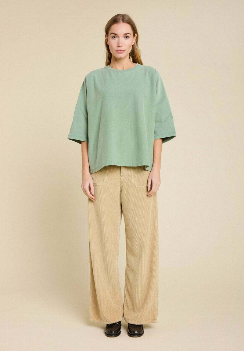Chemise oversize vert clair à manches courtes, associée à un pantalon large encorde beige. Texture lisse et coupe décontractée.