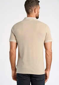 Camisa polo beige de manga corta, con un ribete blanco en el cuello y los puños de las mangas. Textura suave, ajuste casual.