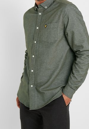 Grön flanellskjorta med knappar och långa ärmar, bröstficka och broderad logotyp. Har en texturerad, mjuk tyg och vita knappar.