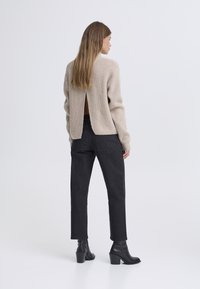 Beige knitted sweater with a back slit, paired with black high-waisted trousers and black heeled ankle boots. Smooth texture, relaxed fit.