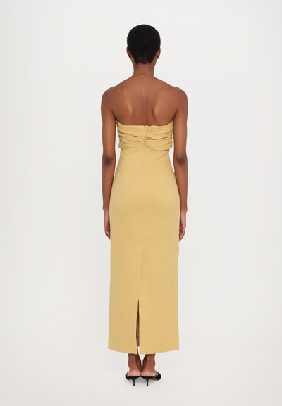 Hüftfreies gelbes Kleid mit gerafftem Stoffdetail am Rücken, figurbetonte Silhouette und einem seitlichen Schlitz bis zur Oberschenkelmitte am Saum.