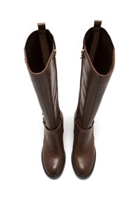 Botas de cuero marrón hasta la rodilla con un acabado suave, puntera redondeada y cremalleras laterales. Acabadas con una hebilla en la correa debajo de la pantorrilla.