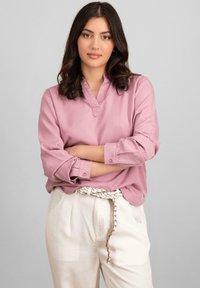 Blouse rose clair à manches longues avec un décolleté en V et des manches retroussées, assortie à un pantalon plissé taille haute de couleur crème.
