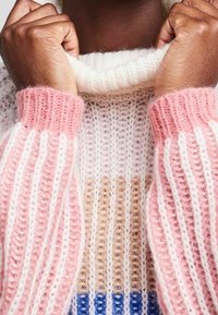 Stickad tröja med randig design i rosa, vitt, beige och blått. Tyget har en mjuk textur med hög krage och ribbade manschetter.