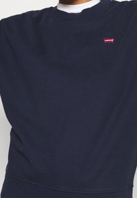 Tmavě modrá bavlněná mikina s kulatým výstřihem, žebrovanými manžetami a malým červeným logem Levi's na hrudi. Hladká textura s klasickým střihem.