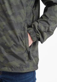 Water-resistant jacket in dark gray with a green dotted camouflage pattern. Features elastic cuffs and a side zippered pocket.