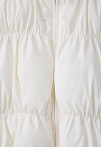 Gros plan d'un tissu matelassé blanc avec des coutures froncées et un détail de couture verticale au centre.