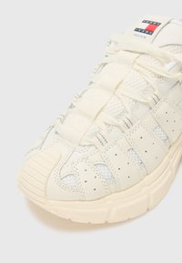 Sneaker de couleur crème avec des panneaux en maille et du cuir texturé. Dotée d'un système de laçage, d'une semelle en caoutchouc et d'une étiquette de marque sur la languette.