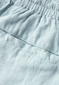 Světlomodrá texturová tkanina se shromážděným elastickým pasem. Má jemný vzor a šité švy, které zdůrazňují měkkost a flexibilitu.