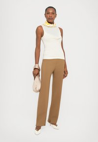 Light cream sleeveless top with draped design; brown tailored trousers; yellow and white patterned scarf; beige handbag; white pointed heels.