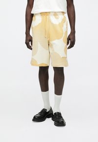 Pantalones cortos con estampado amarillo y crema, con cintura elástica y cordón, hechos de un tejido suave. Llevados con calcetines blancos y zapatos negros.