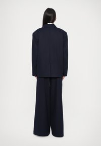Marineblauer, übergroßer Blazer mit strukturierten Schultern, kombiniert mit Hose in weiter Beinform. Glattes Material; simples Design, keine sichtbaren Muster oder Beschläge.