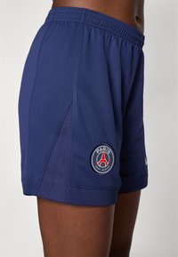 Navy athletic shorts made of textured fabric, featuring an elastic waistband and a logo patch of Paris Saint-Germain on the left leg.