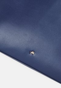 Surface en cuir bleu foncé lisse avec un petit logo métallique doré centré près du bord inférieur.