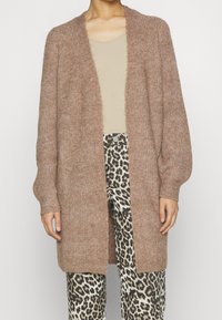 Brun stickad cardigan med mjuk, strukturerad yta, öppen front och långa ärmar, i kombination med byxor i leopardskjortmönster.