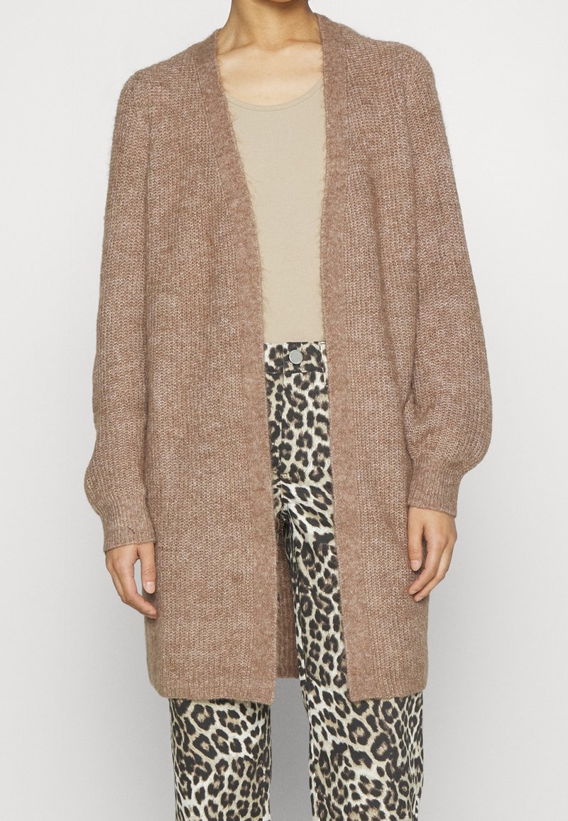 Brun stickad cardigan med mjuk, strukturerad yta, öppen front och långa ärmar, i kombination med byxor i leopardskjortmönster.