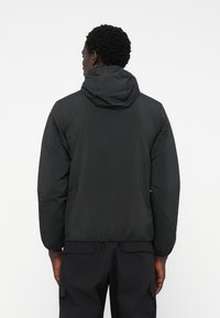 Chaqueta de plumas con capucha negra, de textura ligera y suave. Presenta puños elásticos y una cintura ajustada para una silueta estilizada.