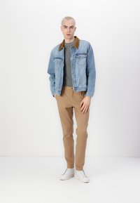 Light blue denim jacket with a brown corduroy collar, gray shirt, tan trousers, and white sneakers. Simple design, regular fit, and smooth texture.