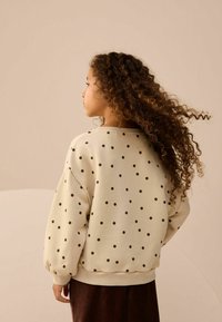 Lys beige sweatshirt med store sorte prikker, med faldne skuldre og ribbede manchetter, set fra ryggen.