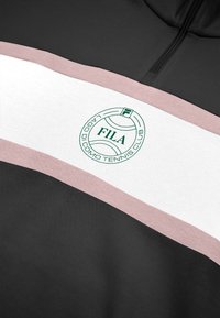 Black sweatshirt with white and blush pink horizontal stripes. Features a green FILA logo within a circular tennis motif. Soft texture.