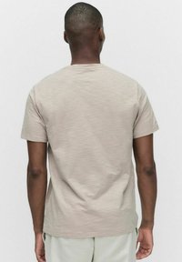 Kortærmet, lys beige t-shirt i et tekstureret stof. Enkel crew neck design med en afslappet pasform, set fra ryggen mod en neutral baggrund.