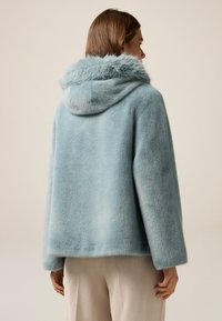 Giacca in pelliccia sintetica di colore azzurro chiaro con cappuccio, caratterizzata da una texture morbida e una forma leggermente oversize, completata da una vestibilità rilassata.