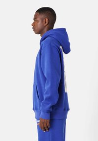 Sudadera azul de tejido suave, con un gran bolsillo frontal, capucha con cordón y un atrevido texto blanco a lo largo del costado.