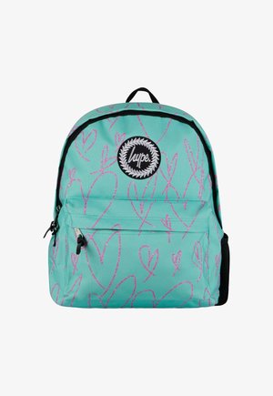 Turkoosi reppu, jossa on vaaleanpunaisia sydänkuvioita, mustia aksentteja ja pyöreä logo-patch. Varustettu päävetoketjulla ja etutaskulla.