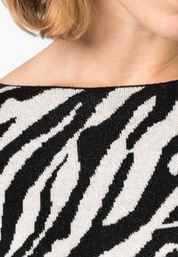 Svartvit randig stickad tröja med bred ringning, med en texturerad tyg och ett horisontellt mönster som liknar djurens ränder.
