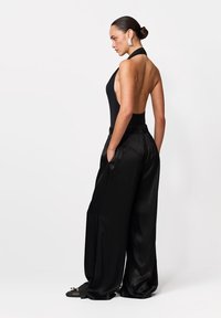 Czarny kombinezon na szyję z odkrytymi plecami, zestawiony z szerokimi, czarnymi spodniami. Charakteryzuje się gładkim materiałem i luźnym krojem.