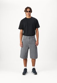 T-shirt en coton noir associé à un short en denim gris. Le short a une coupe décontractée, tandis que les chaussures sont sombres avec des accents blancs. Lunettes de soleil incluses.