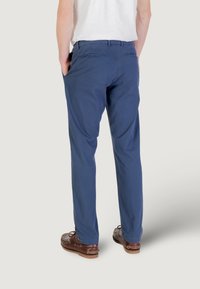 Pantaloni blu navy con una vestibilità rilassata, realizzati in un tessuto leggero. Presentano due tasche posteriori e una texture liscia. Scarpe marroni visibili.
