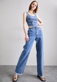 Cropped top od trapera i plave traperice viskog struka sa širokim krojem. Traperice imaju razderane rubove i detalj elastične struk. 