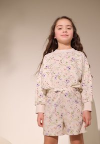 Ubranie w kwiatowy wzór składające się z bluzki z długim rękawem i szortów, wykonane z miękkiego materiału w odcieniu beżowym, z różowymi, fioletowymi i zielonymi akcentami.