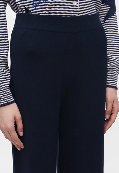 Pantalon bleu marine taille haute porté avec un haut boutonné à manches longues rayé bleu marine et blanc.