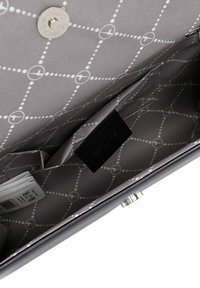 Interiores grises de una bolsa con un patrón geométrico, una etiqueta negra y compartimentos para organización. Cierre a presión visible.