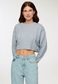 Maglione corto azzurro chiaro con motivo a trecce e colletto a costine, abbinato a jeans azzurro chiaro a vita alta con un leggero sbiadimento.