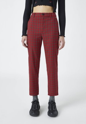 Osoba nosząca czerwone spodnie w kratę z wysokim stanem, szare skarpetki, czarne trampki i krótki czarny top z długim rękawem z małym czerwonym haftem.