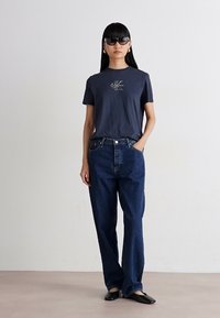 Navy blue t-shirt with a small logo, paired with loose-fitting blue denim jeans and black flats. Smooth fabric, casual fit, minimal design.