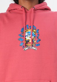 Roze hoodie met een grafisch ontwerp dat een blauwe karakter, ronde accenten en tekst bevat. Het materiaal is zacht, met een relaxte pasvorm en een trekkoordkap.